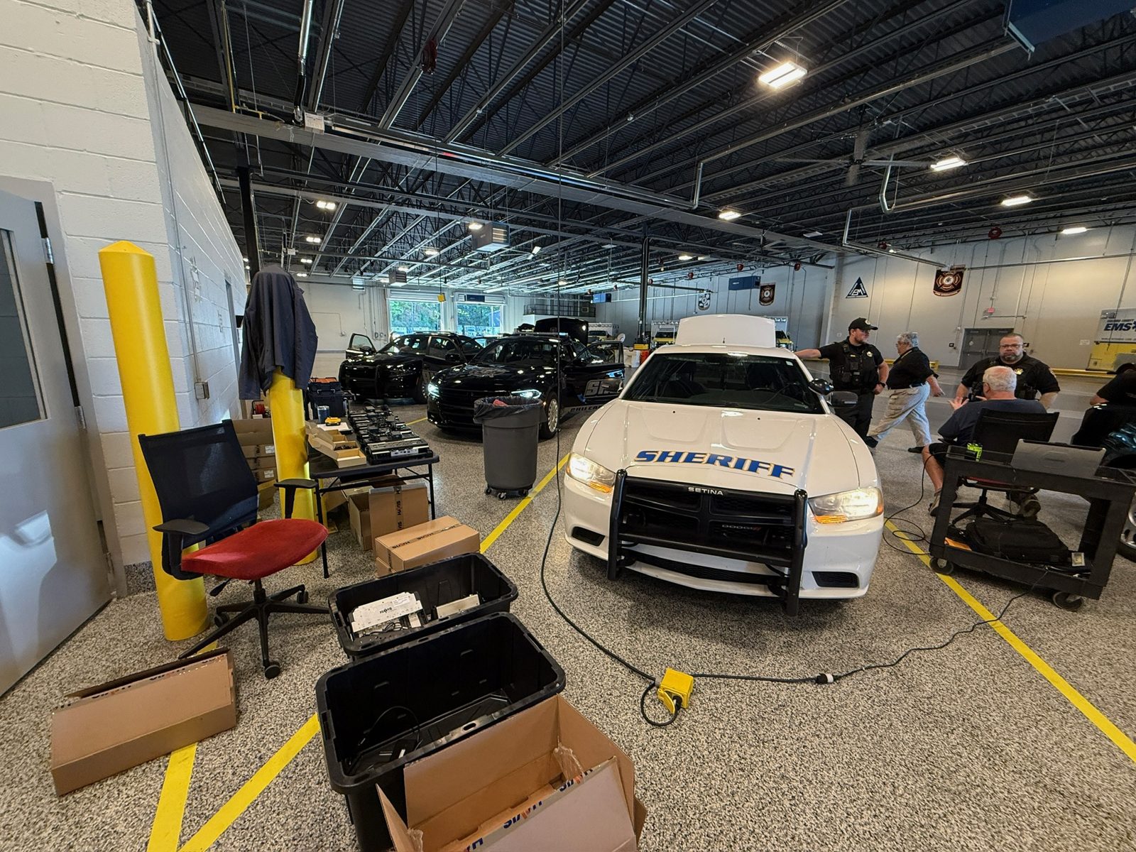 Shop bay with a Sheriff patrol vehicle and patrol cars, technicians at work.